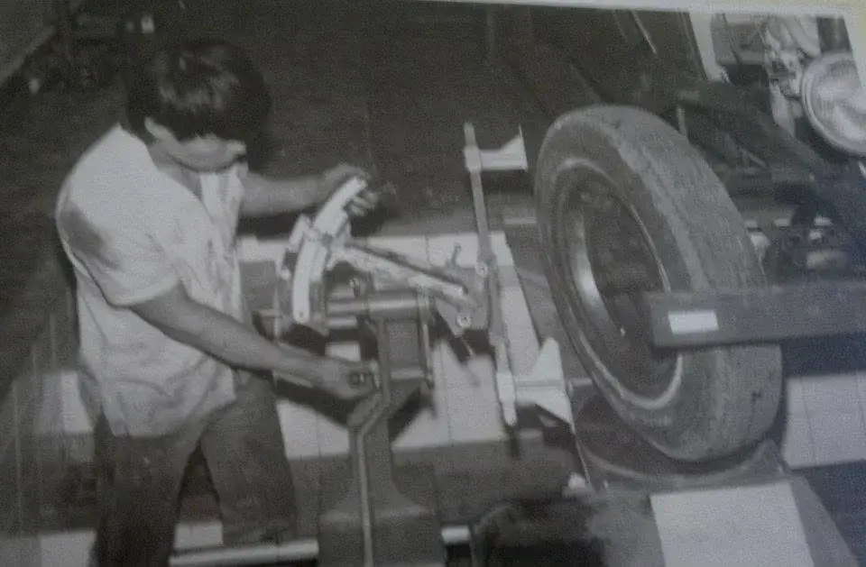 Rapaz de camisa clara ajustando uma máquina antiga presa à roda de um carro