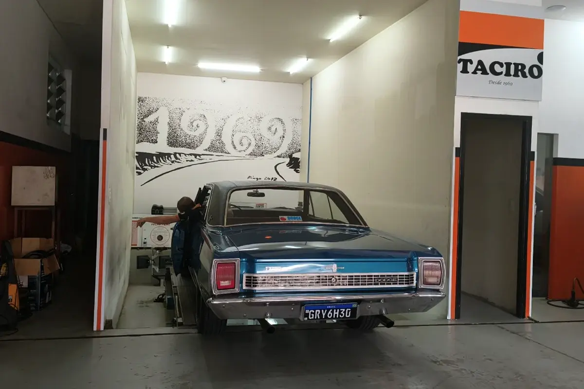 Dodge azul clássico posicionado sobre o alinhador Hunter da Taciro, de frente para o mural de 1969 e embaixo da placa Desde 1969