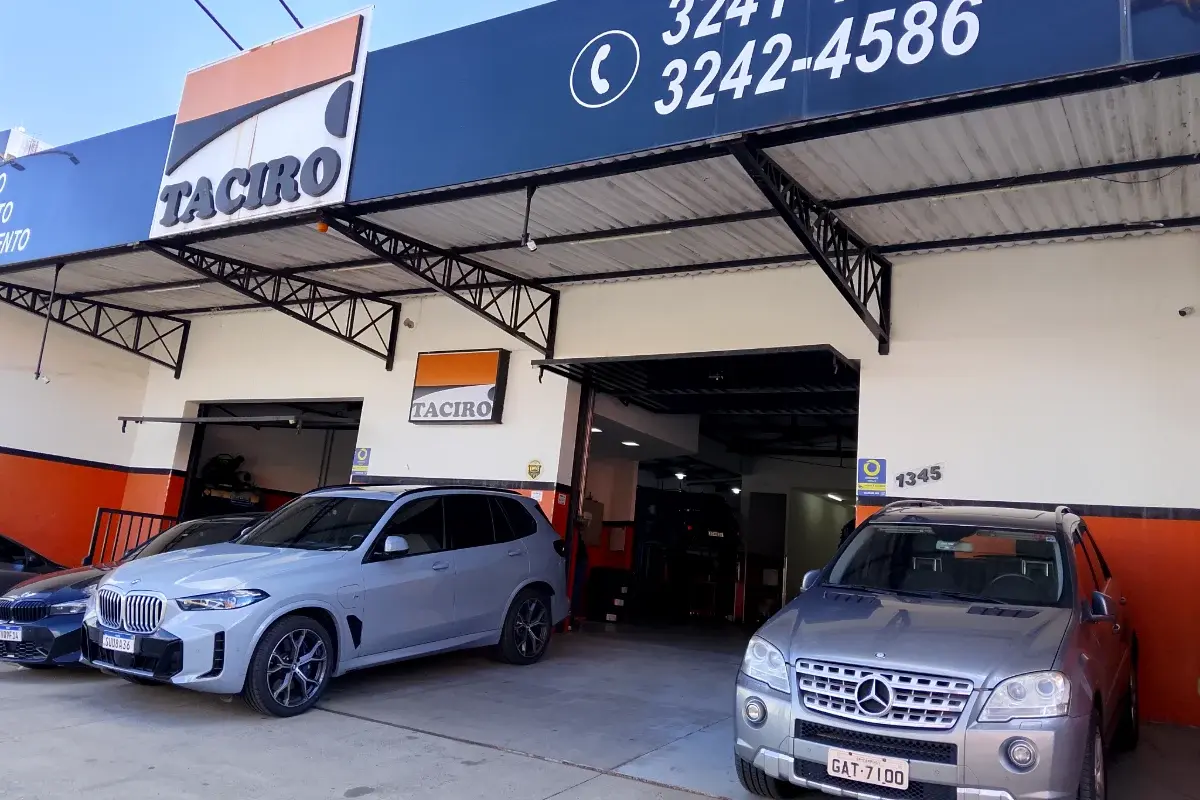 Entrada da Taciro vista da calçada, com um BMW X5 e uma Mercedes estacionados embaixo do letreiro da oficina