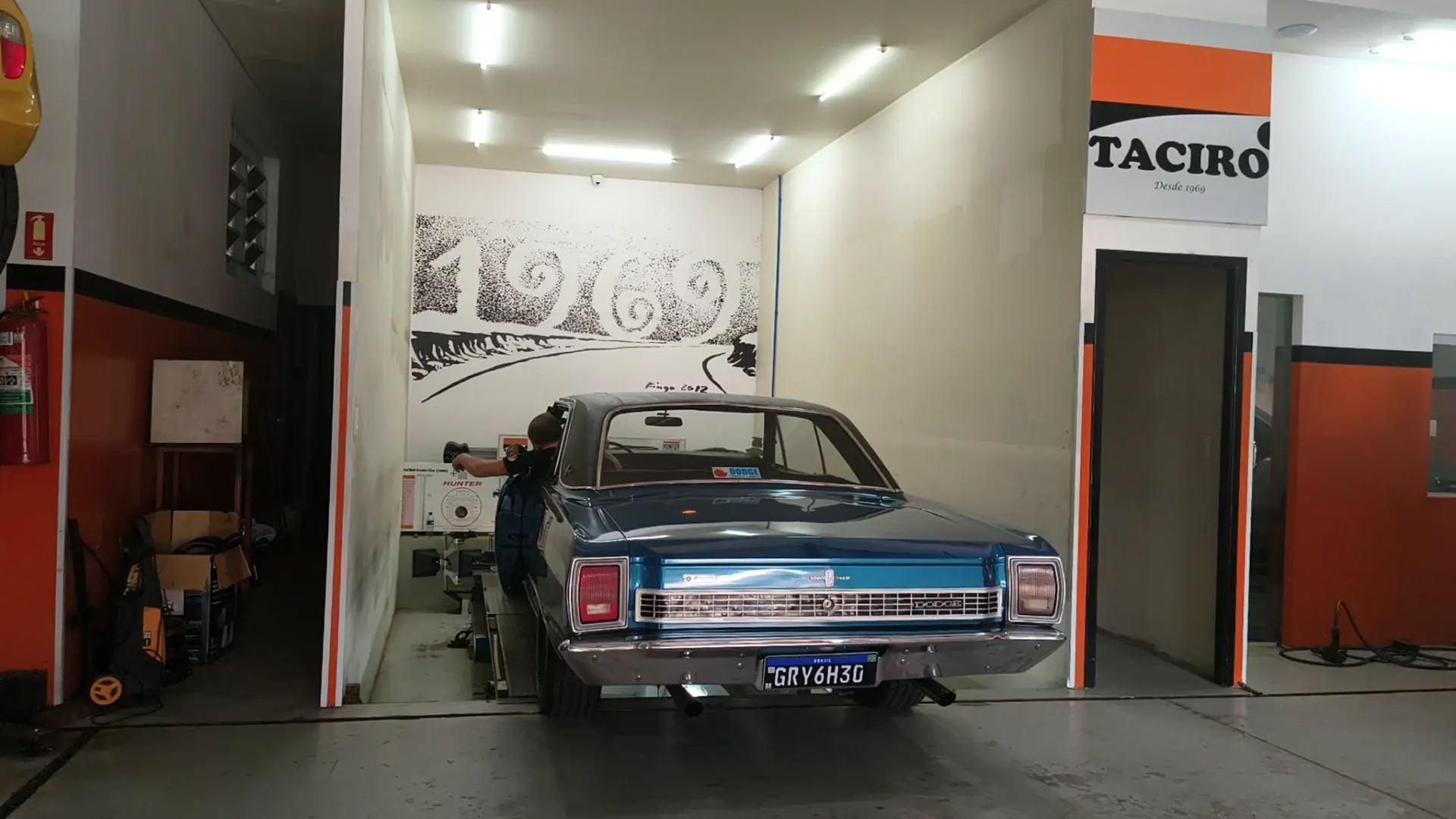 Dodge azul clássico sobre o alinhador Hunter da Taciro, na sala onde o ano de 1969 está pintado na parede