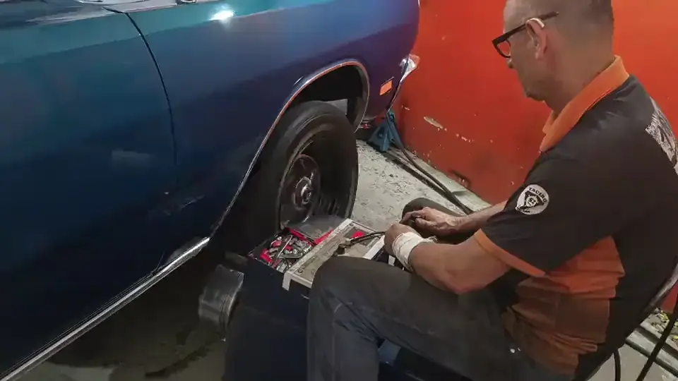 Mecânico da Taciro sentado ao lado da roda dianteira de um Dodge azul, com a máquina de balanceamento encostada no pneu
