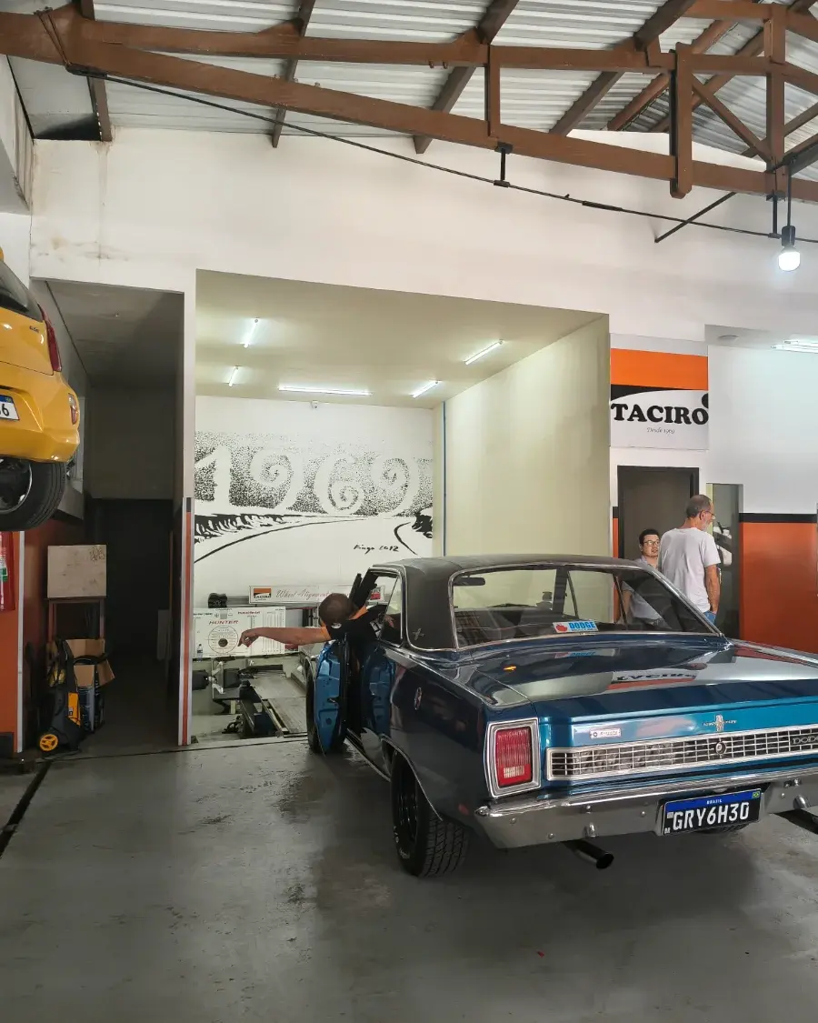 O ano de 1969 pintado na parede da sala de alinhamento da Taciro, com um Dodge clássico entrando e a placa Desde 1969 na parede ao lado